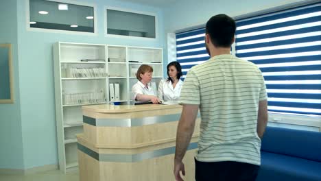 Two-nurses-working-at-reception-desk-greeting-male-patient