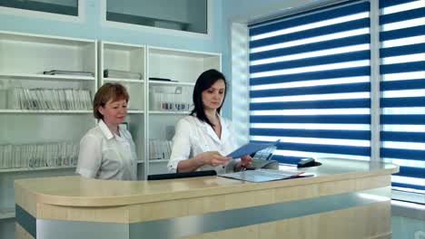 Smiling-female-doctors-standing-at-the-reception-desk-in-hospital