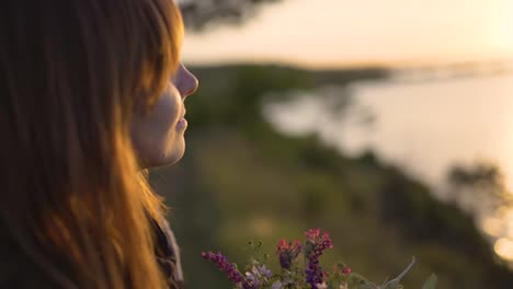 beautiful-young-woman-with-a-bouquet-of-wildflowers-on-the-coast-at-sunset