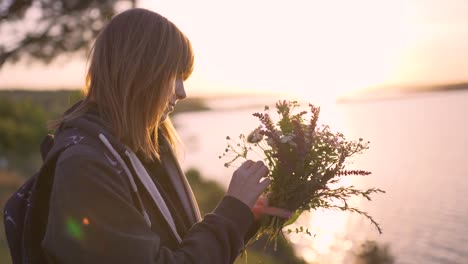 beautiful-young-woman-with-a-bouquet-of-wildflowers-on-the-coast-at-sunset