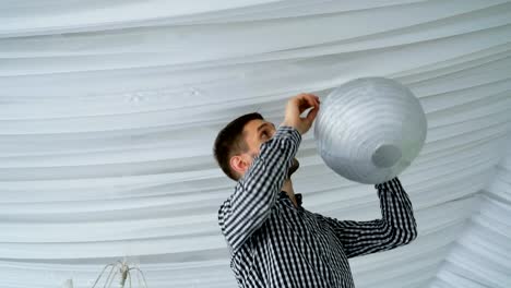 Man-hanging-colorful-white-pink-gray-paper-lanterns-to-ceiling.