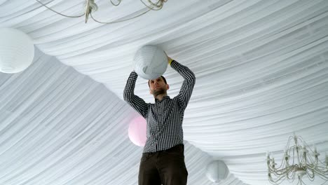 Man-hanging-colorful-white-pink-gray-paper-lanterns-to-ceiling.