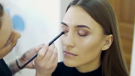 Wedding-makeup-artist-making-a-make-up-for-bride.-Beautiful-sexy-model-girl-indoors.-Beauty-woman-with-curly-hair.-Female-portrait.-Bridal-morning-of-a-cute-lady.-Close-up-hands-near-face