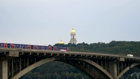 Zug-fährt-über-die-Brücke-gegen-den-Himmel-und-die-Kuppeln-der-Kirche.-City-u-Bahn-links-außen.-Öffentlichen-Verkehrsmitteln-unterwegs.-Autos-fahren-über-die-Brücke-über-den-Fluss.