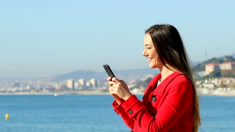 Glückliche-Frau-SMS-auf-Handy-am-Strand-im-winter