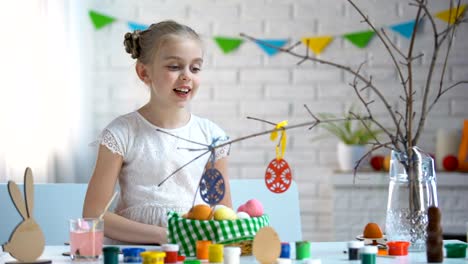 Little-girl-hanging-hand-made-toy-eggs-on-tree-branches,-Easter-decoration