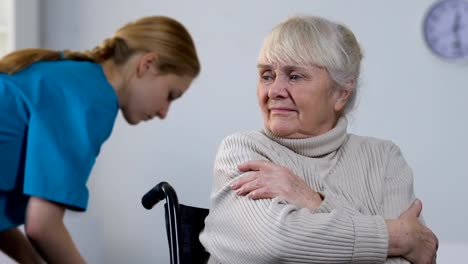 Hilfreiche-junge-Krankenschwester-für-Behinderte-Dame-im-Rollstuhl-mit-warmen-Plaid,-Pflege