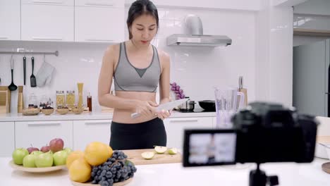 Blogger-deportiva-mujer-asiática-con-cámara-de-grabación-cómo-realizar-el-video-de-jugo-de-manzana-para-su-abonado,-mujer-frutas-orgánicas-haciendo-jugo-de-manzana-por-ella-misma-en-casa.-Concepto-de-comida-sana.