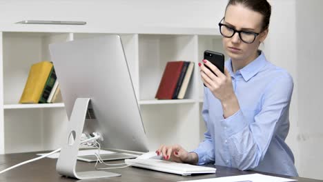 Junges-Mädchen-mit-Smartphone-während-der-Arbeit-am-Computer