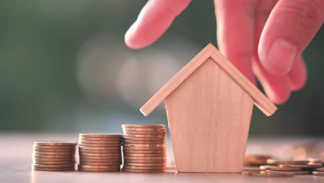 Hand-putting-house-with-Money-coin-on-nature-green-background.-Property-investment-and-house-mortgage-financial,-Credit-home-concept.-Slow-Motion