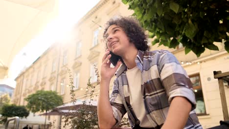 Un-hombre-está-hablando-por-teléfono-y-sonriendo.-Retrato-de-blogger-guapo,-estudiante-al-aire-libre-y-hablar-en-el-teléfono-inteligente-móvil.-Concepto-de-educación,-viajes-y-Turismo