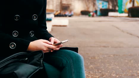 Mädchen-mit-einem-Handy-auf-einer-Bank-im-Stadtpark-im-Frühjahr