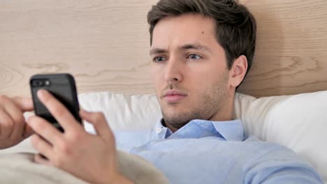 Junger-Mann-mit-Smartphone-in-Bett