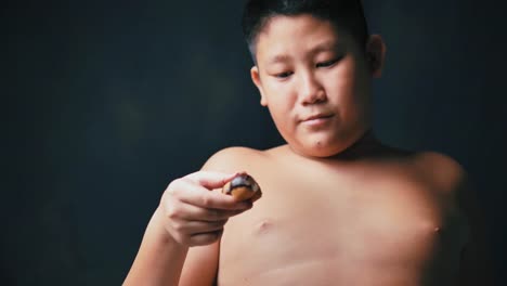 gran-construir-asiático-niño-preadolescente-comiendo-Donut-mientras-toca-su-barriga,-cámara-lenta-en-poca-luz.