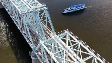 Luftaufnahme-der-Eisenbahnbrücke,-mit-einem-fahrenden-Zug-auf-ihr,-über-den-Fluss,-der-durch-eine-Großstadt-fließt