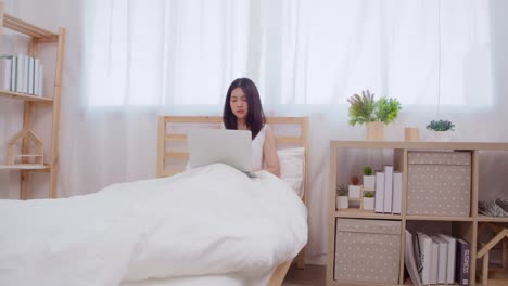 Young-business-freelance-Asian-woman-working-on-laptop-checking-social-media-while-lying-on-the-bed-when-relax-in-bedroom-at-home.-Lifestyle-women-at-house-concept.