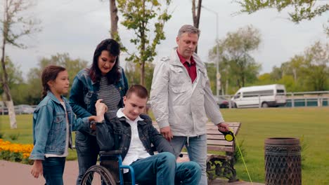 Sister-and-mother-are-taking-brother-in-a-wheelchair.-Happy-family-with-disabled-teenager-together-walking.