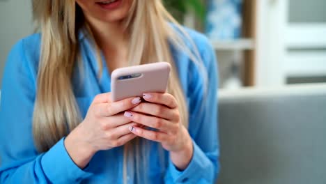 Primer-plano-de-las-manos-de-las-mujeres-sosteniendo-el-teléfono-rosa-celular,-mensajes-de-texto-de-la-chica-usando-la-aplicación-y-viendo-el-video-en-el-teléfono-móvil,-disfrutando-de-la-lectura-de-las-redes-sociales-en-casa.