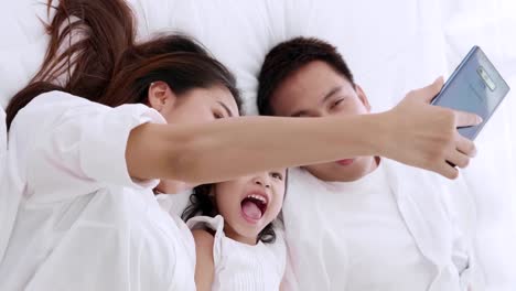 Asiatische-Familie-liegen-über-das-Bett-spielen-und-suchen-Anwendung-Smartphone,-während-im-Schlafzimmer-liegen