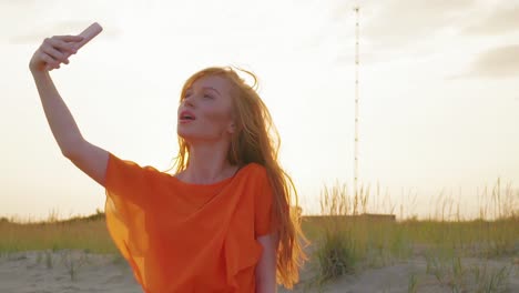 Schöne-Mädchen-nimmt-Selfie-am-Strand-mit-Handy.-Fröhliche-junge-Frau-am-Strand-macht-ein-Selfie-Porträt-bei-Sonnenuntergang