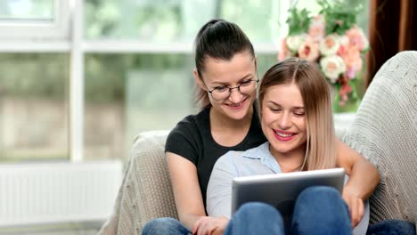 Two-happy-homosexual-woman-relaxing-looking-at-screen-of-tablet-pc-discussing-something