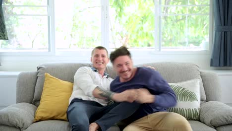 Gay-couple-relaxing-on-couch-watching-tv.-Cheering-and-kissing.