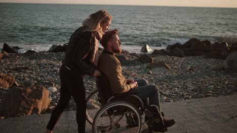 Mujer-cuidando-de-marido-discapacitado-y-caminando-con-él-por-el-mar