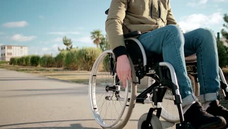 Young-male-wheelchair-user-is-rolling-over-city-streets,-detail-view-of-legs