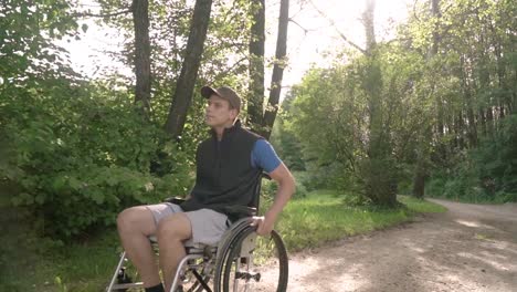 Slowmotion-Frontgesicht-folgen-von-behinderten-jungen-Studenten-Mann-in-einem-Rollstuhl-beobachten-die-Natur-um-ihn-herum,-mit-Sonnenbrand