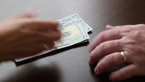 Woman-Counting-One-Hundred-Dollar-Bills-Money-Out-On-Table-For-Man