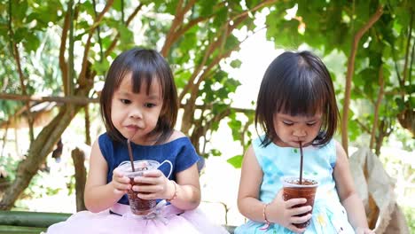 Pequeña-niña-asiática-bebiendo-su-bebida-mientras-está-sentada-en-el-parque-el-día-de-verano.-Enfoque-selectivo.