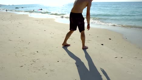 Joven-hombre-gay-en-el-amor-caminando-en-la-playa-tropical-y-el-dibujo-del-corazón-en-la-arena-para-novio