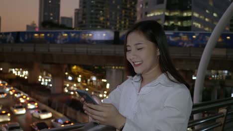 Excited-business-asian-woman-celebrating-good-news-checking-smart-phone-in-the-modern-city-center-in-the-night-of-Bangkok-Thailand.-Concept-Technology-communication,-success-by-mobile-phone