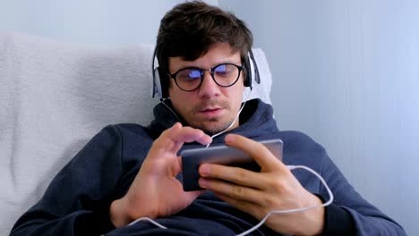 Man-in-glasses-and-headphones-online-browsing-on-smartphone.-Face-close-up.