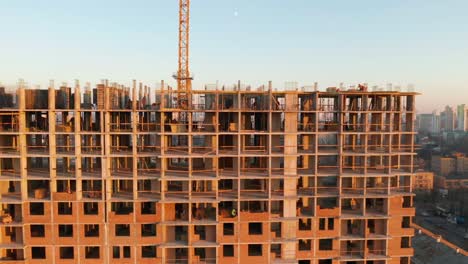 Aerial-Shot-of-the-Building-in-the-Process-of-Construction.-Labor-working-in-big-construction-site.-In-the-Background-Working-Crane-and-city