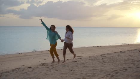 Two-young-happy-women-running-on-the-beach-at-the-sunset-time