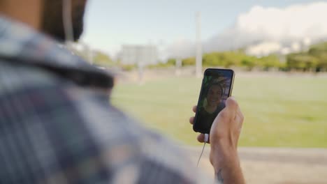 Sobre-la-toma-del-hombro-del-hombre-chateando-en-línea---haciendo-videollamada-en-su-teléfono-inteligente-con-su-amigo-en-el-parque