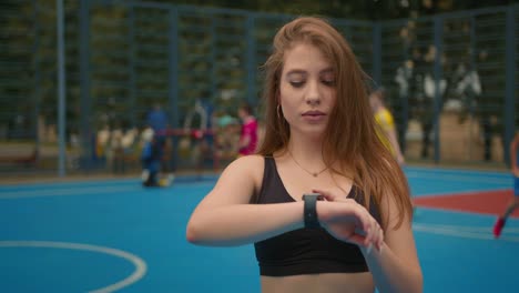 Close-up-shooting.-Portrait-of-a-sports-girl.-The-girl-is-looking-at-the-training-information-on-her-smartwatch.-People-are-playing-floorball-in-the-background.-4K