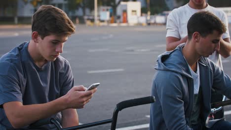 Joven-está-usando-su-teléfono-inteligente-mientras-descansa-sentado-en-bicicleta-bmx-después-de-entrenar-con-amigos