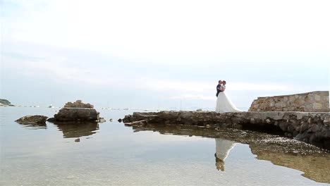 Mann-und-Frau-in-der-formalen-Kleidung-küssen-am-alten-Pier-auf-dem-Seeweg.-Bräutigam,-Braut-Hochzeit-Kleid-umarmt-ihre-Stellung-am-alten-Burgruinen-dock-in-der-Nähe-von-See-Wasser-Spiegelung---Yacht-Boote-Hintergrund-geht