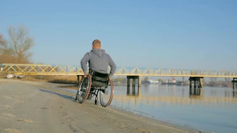 Disabled-person-in-a-wheelchair,-back-view,--goes-along-embankment-