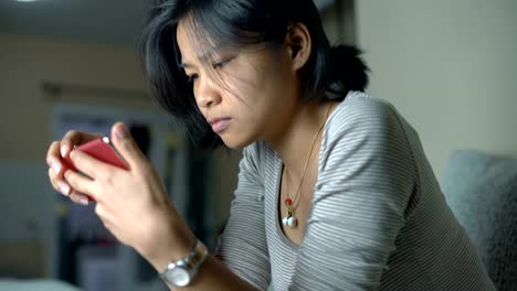 Young-Thai-girl-using-smart-phone-in-living-room