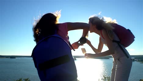 Happy-Female-Couple-Drinking-Champagne-on-a-High-Rock-in-the-Sunshine