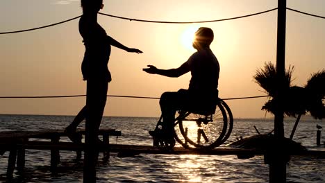 romantic-date-of-female-with-male-invalid-on-wheelchair-on-jetty-near-sea-against-summer-sunset