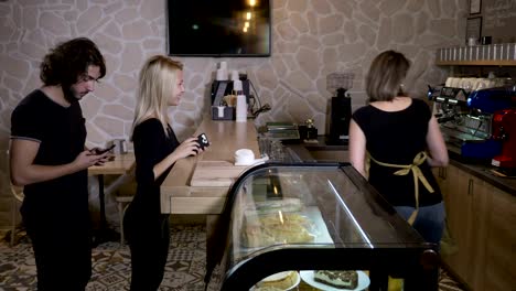 Young-and-beautiful-customers-in-a-coffee-shop-ordering-drinks-and-paying-with-cryptocurrency-bitcoin-using-their-smartphone