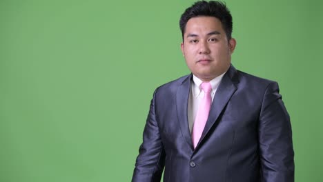 Young-handsome-overweight-Asian-businessman-against-green-background