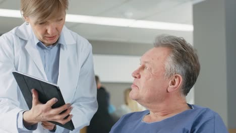 En-el-Hospital-femenino-médico-muestra-Tablet-PC-al-paciente-mayor,-explicando-su-condición.-Moderno-Hospital-con-la-mejor-atención-posible.