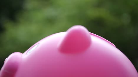 Hand-putting-coins-in-a-pink-piggy-bank,-saving-money-concept