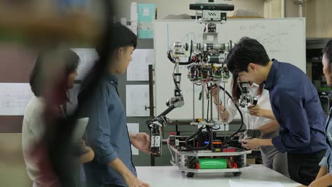 Electrónica-de-joven-ingeniero-equipo-colaborando-en-la-construcción-del-robot-en-el-taller.-Ingeniero-de-equipo-pone-en-marcha-proyecto-de-robot-juntos.-Personas-con-el-concepto-de-tecnología-o-innovación.