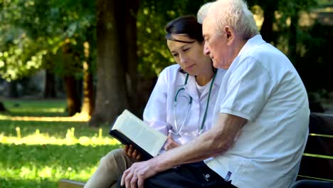 Una-niñera,-enfermera,-cuidar-a-los-ancianos-una-chica-(mujer)-y-el-abuelo-se-sientan-en-un-libro-y-leer-un-libro,-en-el-parque.